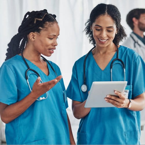 Zwei Pflegefachkräfte mit Stethoskopen schauen auf ein Tablet