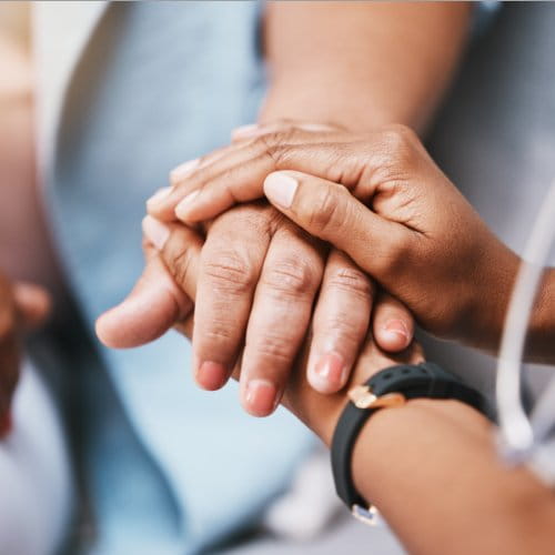 Pflegekraft hält mit beiden Händen die Hand einer älteren Patientin